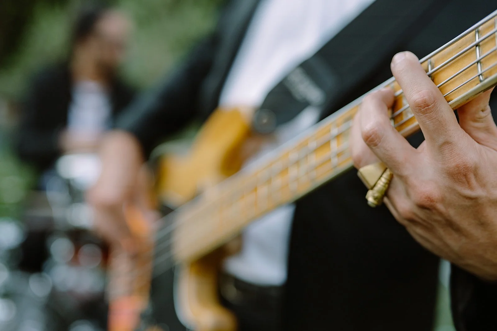 Close-up of a person's hand playing an electric guitar with a woman singing in the blurred background.