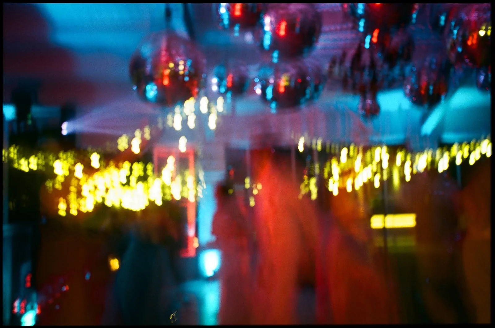 Blurred image of a party or nightclub with neon lights, disco balls, and colorful decorations.