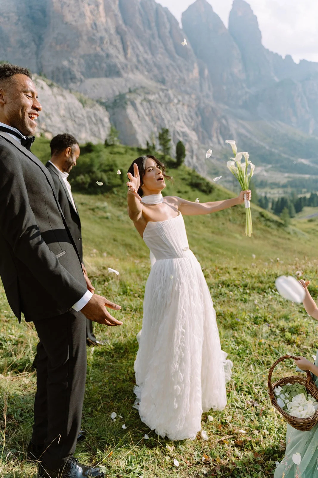 Bride tossing flower petals during outdoor wedding ceremony with mountains in the background.