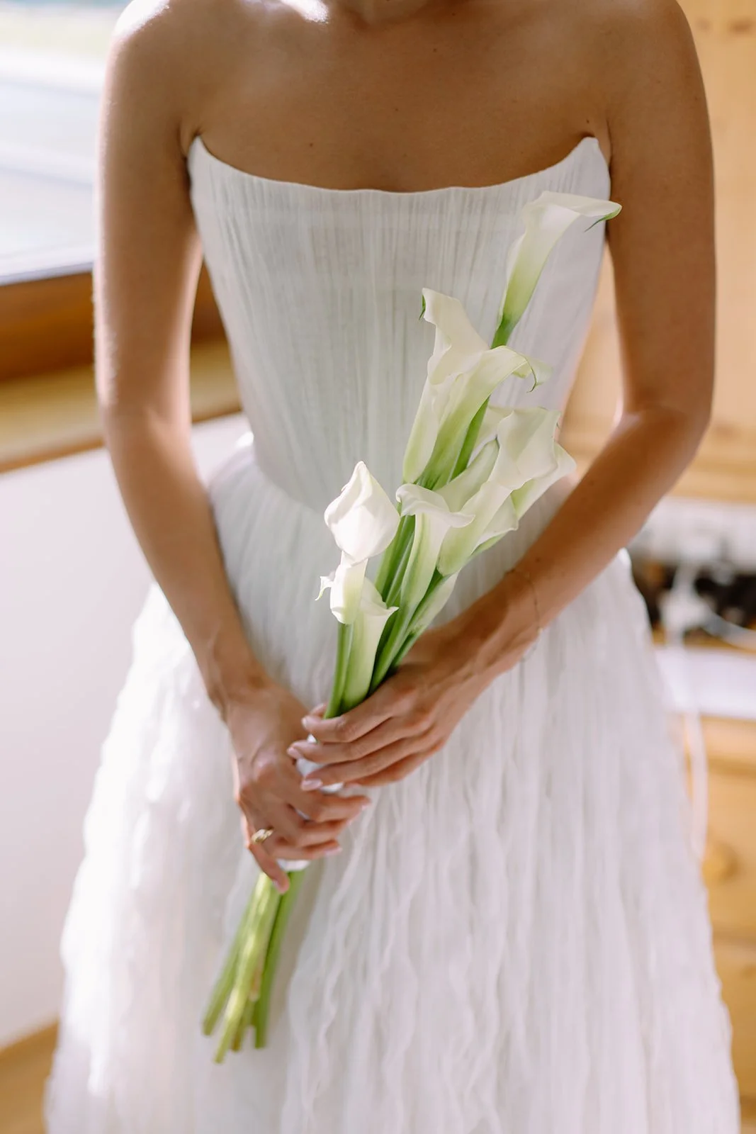 A woman in a white strapless dress holding a bouquet of white calla lilies.