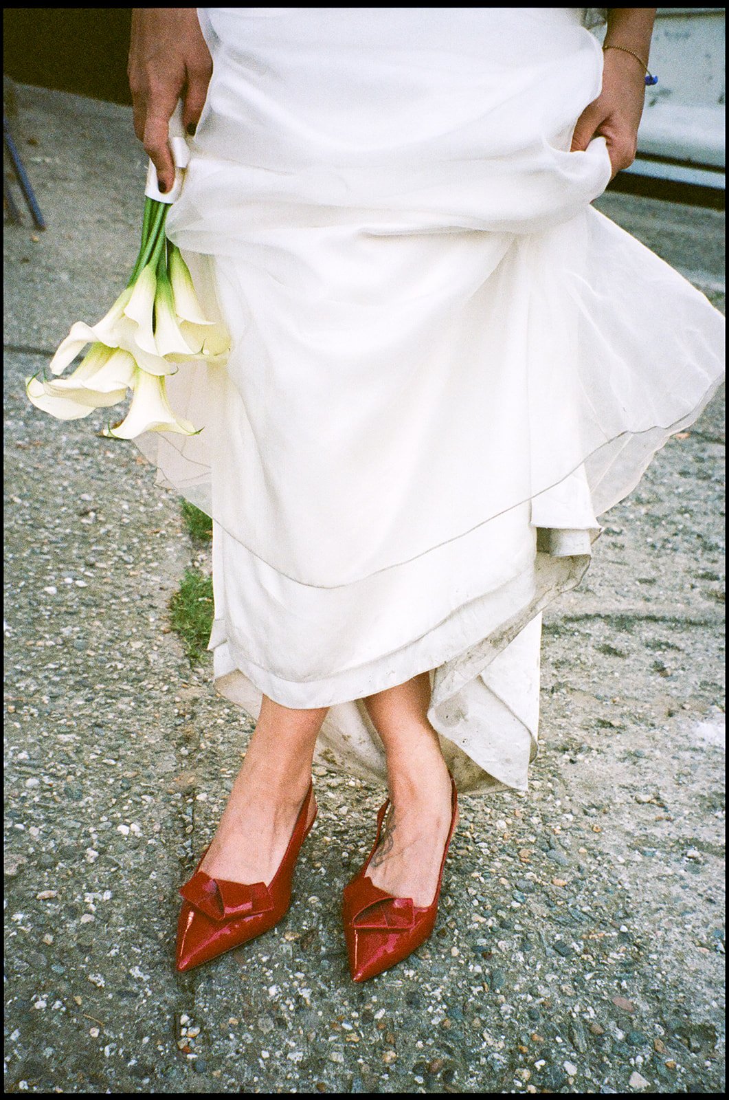 Person in a wedding dress holding white calla lilies, wearing red high heels with bows.
