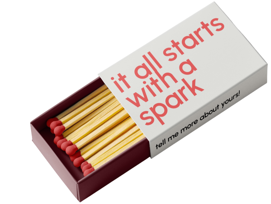 An open matchbox with several matches inside, with red tips. The matchbox has a white label with red text that reads 'it all starts with a spark' and black text underneath that says 'tell me more about yours!'