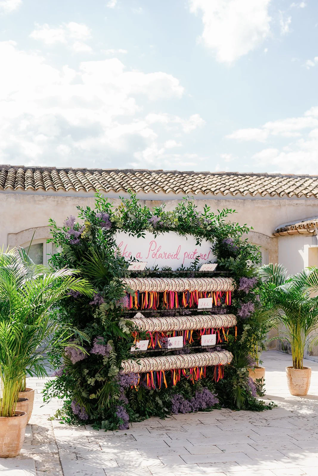 A decorative outdoor setup with a large floral arrangement, ribbons, and a sign that reads 'like a Polaroid picture!'.
