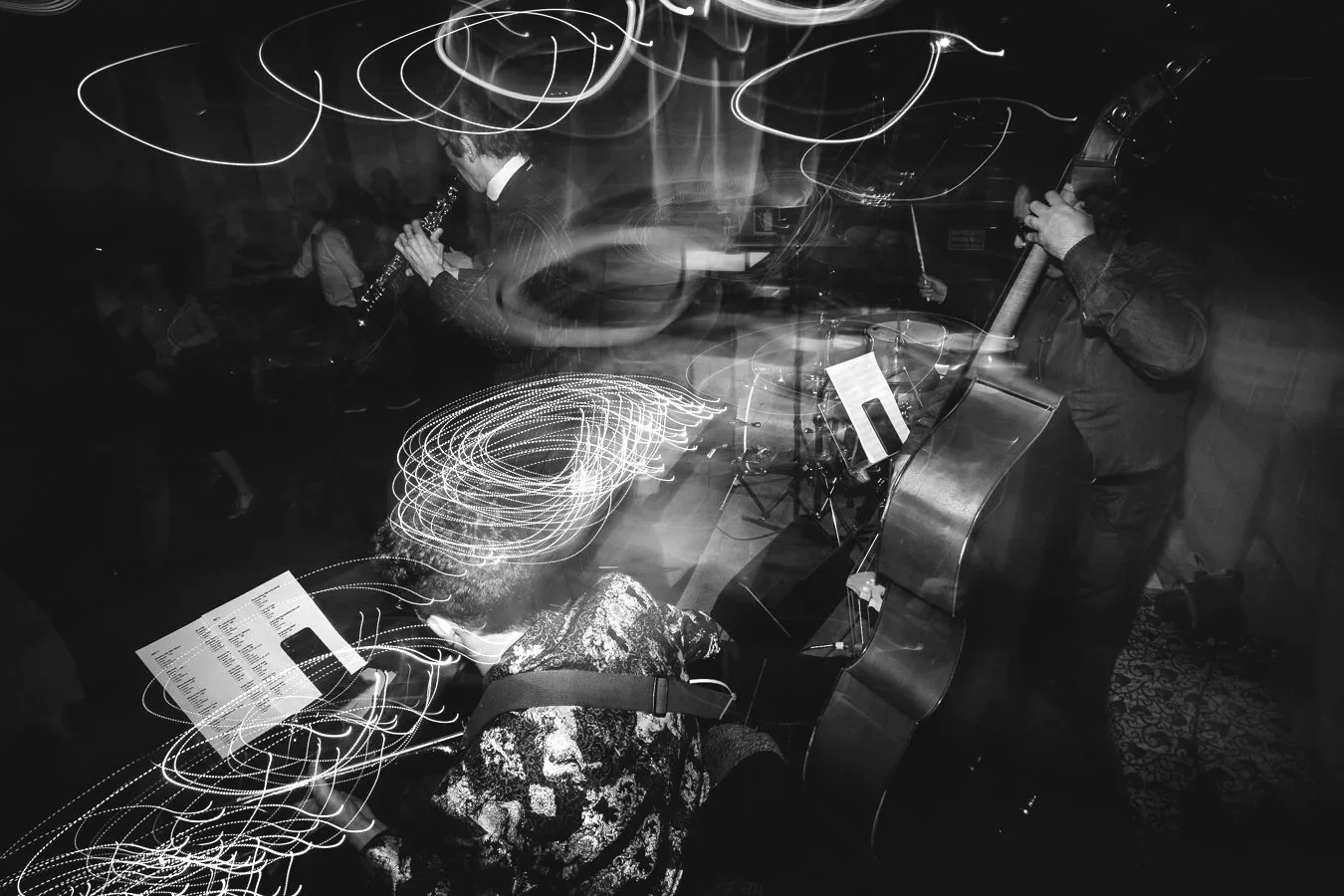 Musicians playing instruments on stage during a performance, with light trails creating a dynamic, swirling effect in a dark venue.