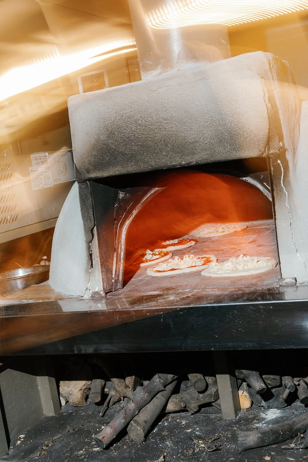 Pizza baking inside a wood-fired oven with a fire burning inside, seen from the front.