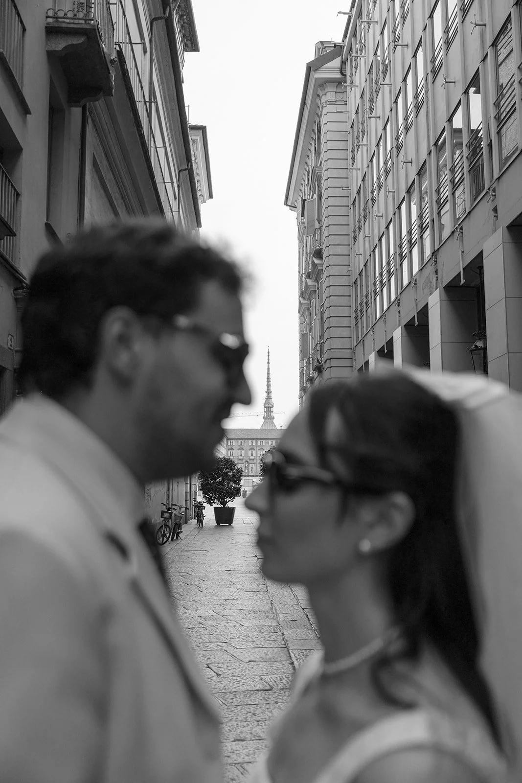 Black and white photo of a couple facing each other on a city street, with a distant tower visible in the background.