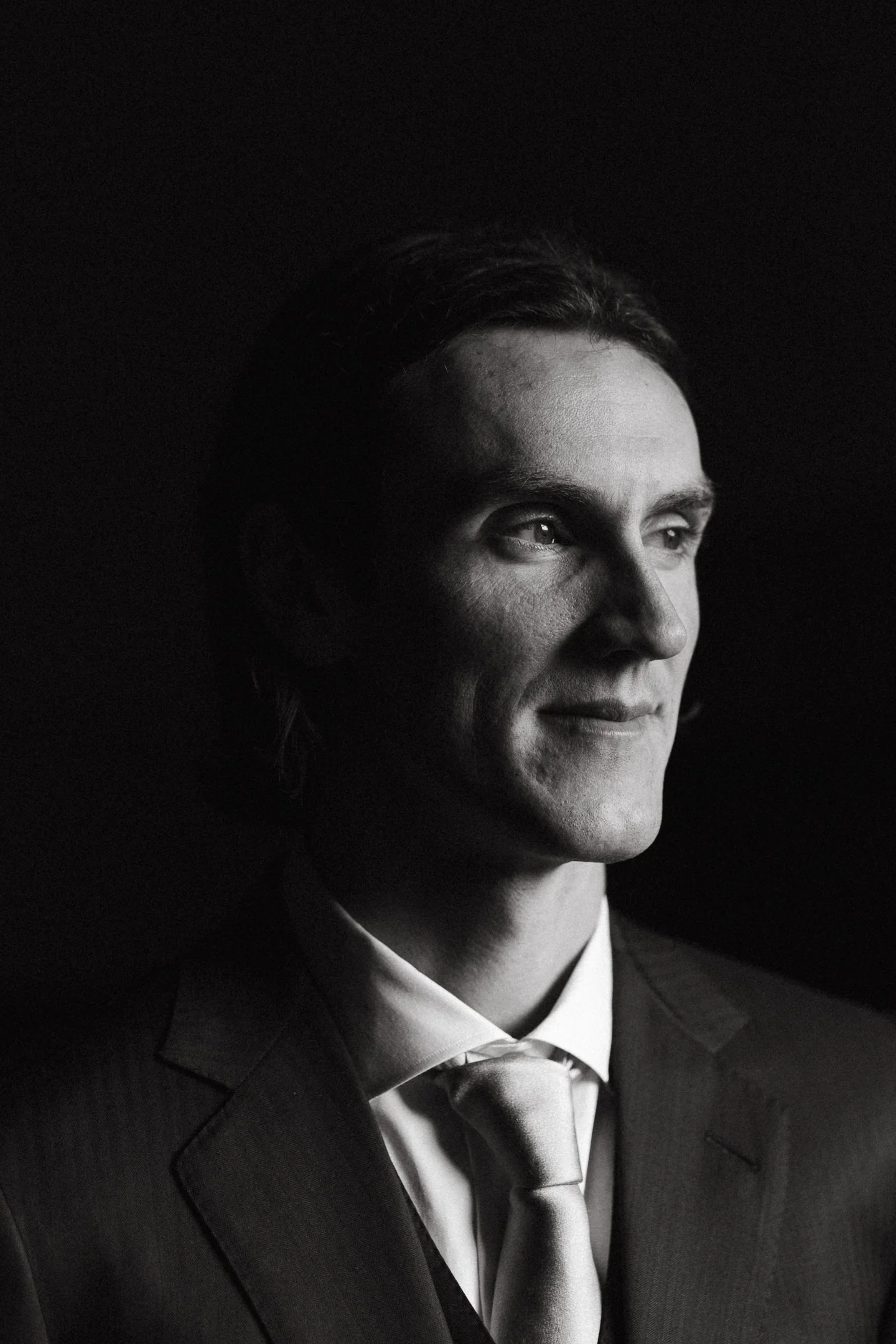 A black-and-white portrait of a man in a suit, looking slightly to the right, with soft lighting highlighting his facial features.