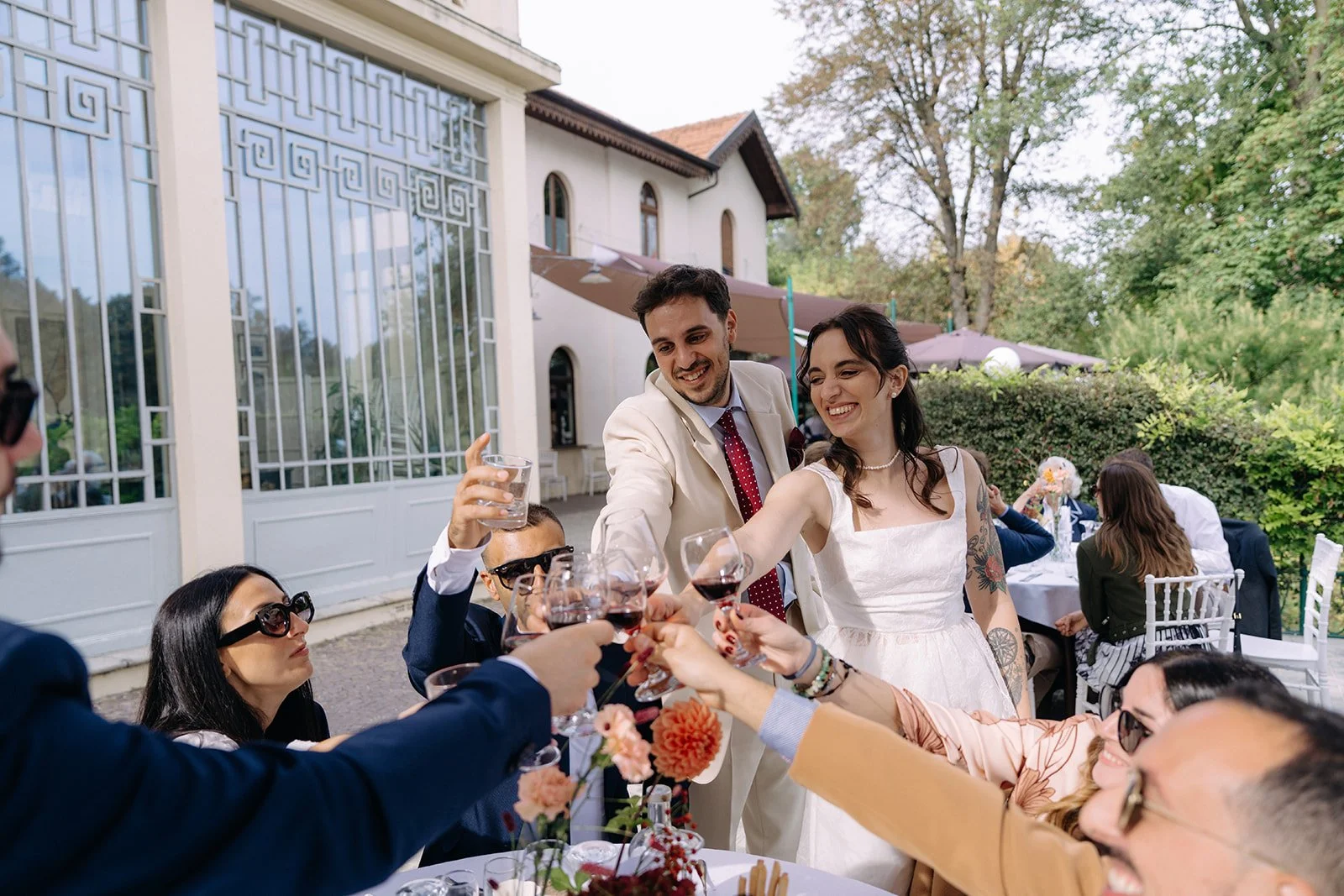 A group of friends celebrating at an outdoor wedding reception, raising glasses for a toast, with a bride and groom smiling in the center.