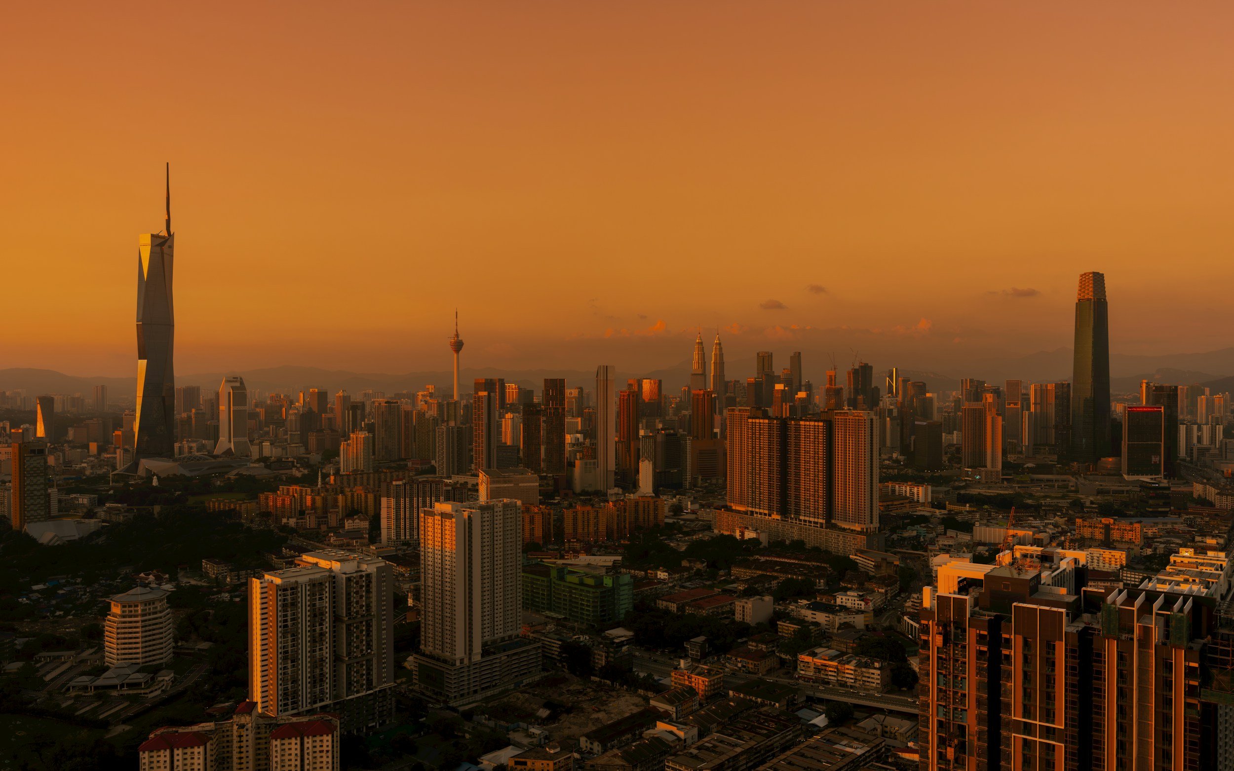 Skyline of a city at sunset with tall skyscrapers and a mountain range in the background.