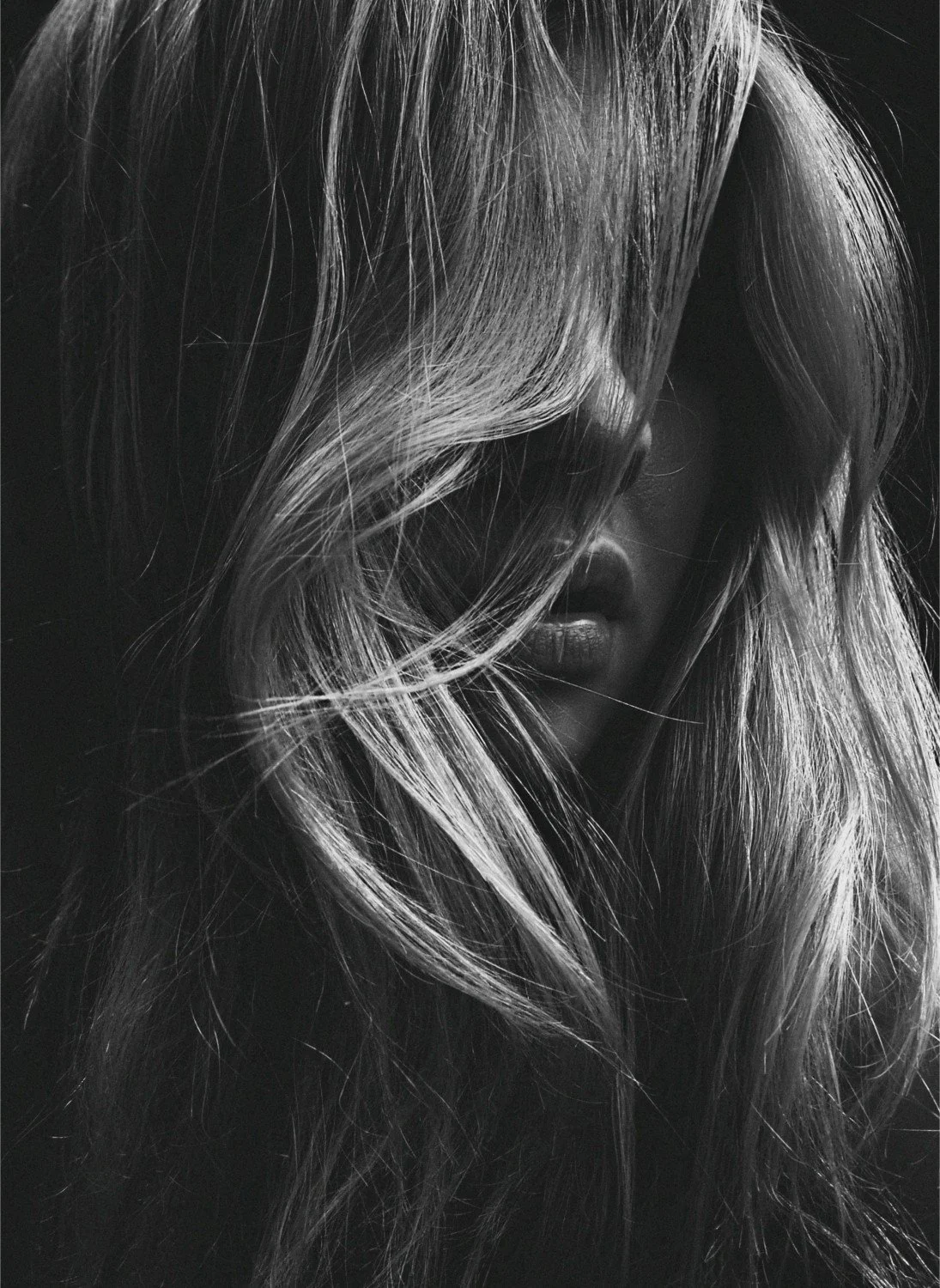 Black and white photograph of a woman with long, wavy hair partially covering her face.
