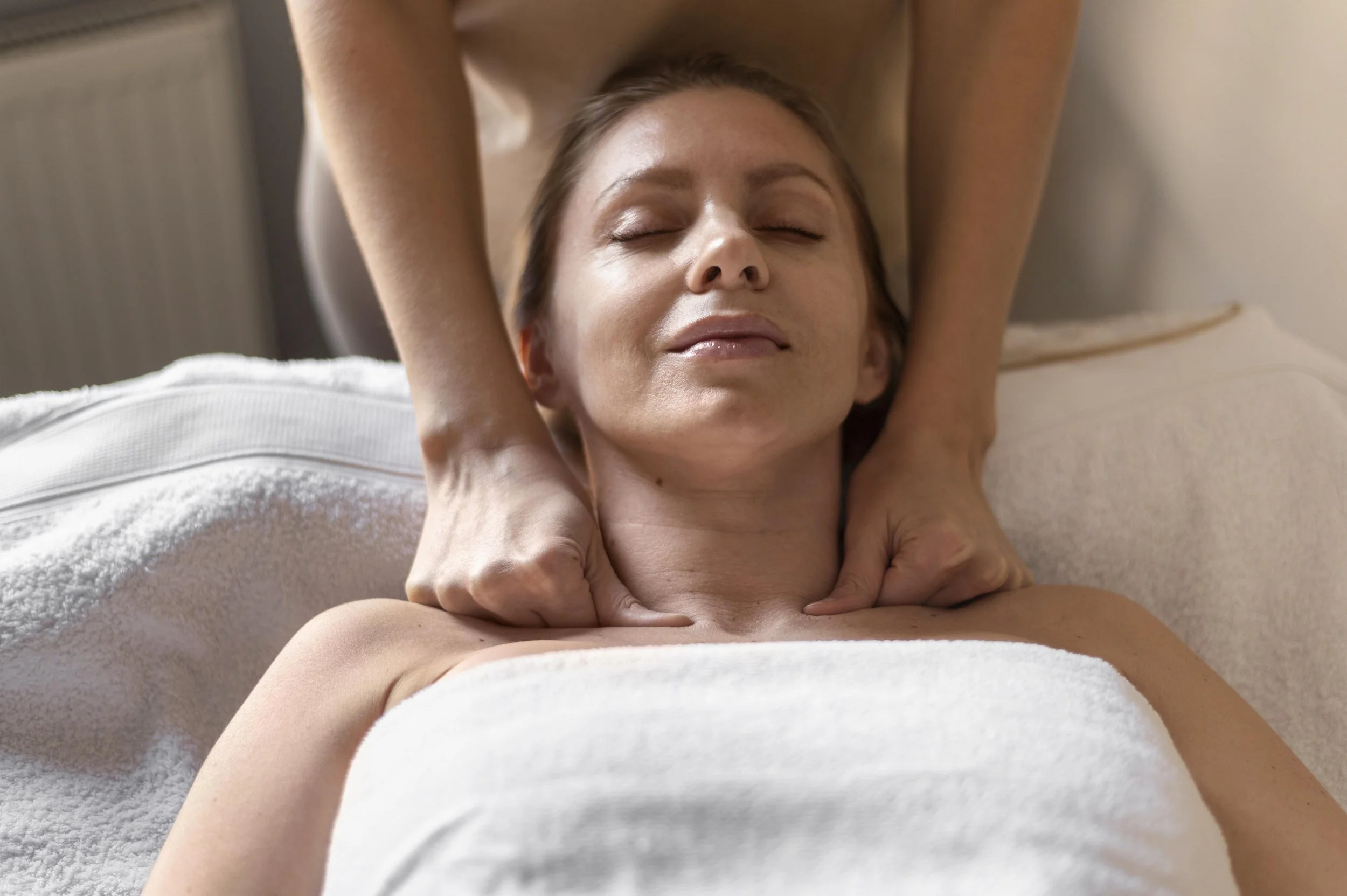 Woman receiving a neck and shoulder massage while lying down on a massage table with a towel covering her chest.
