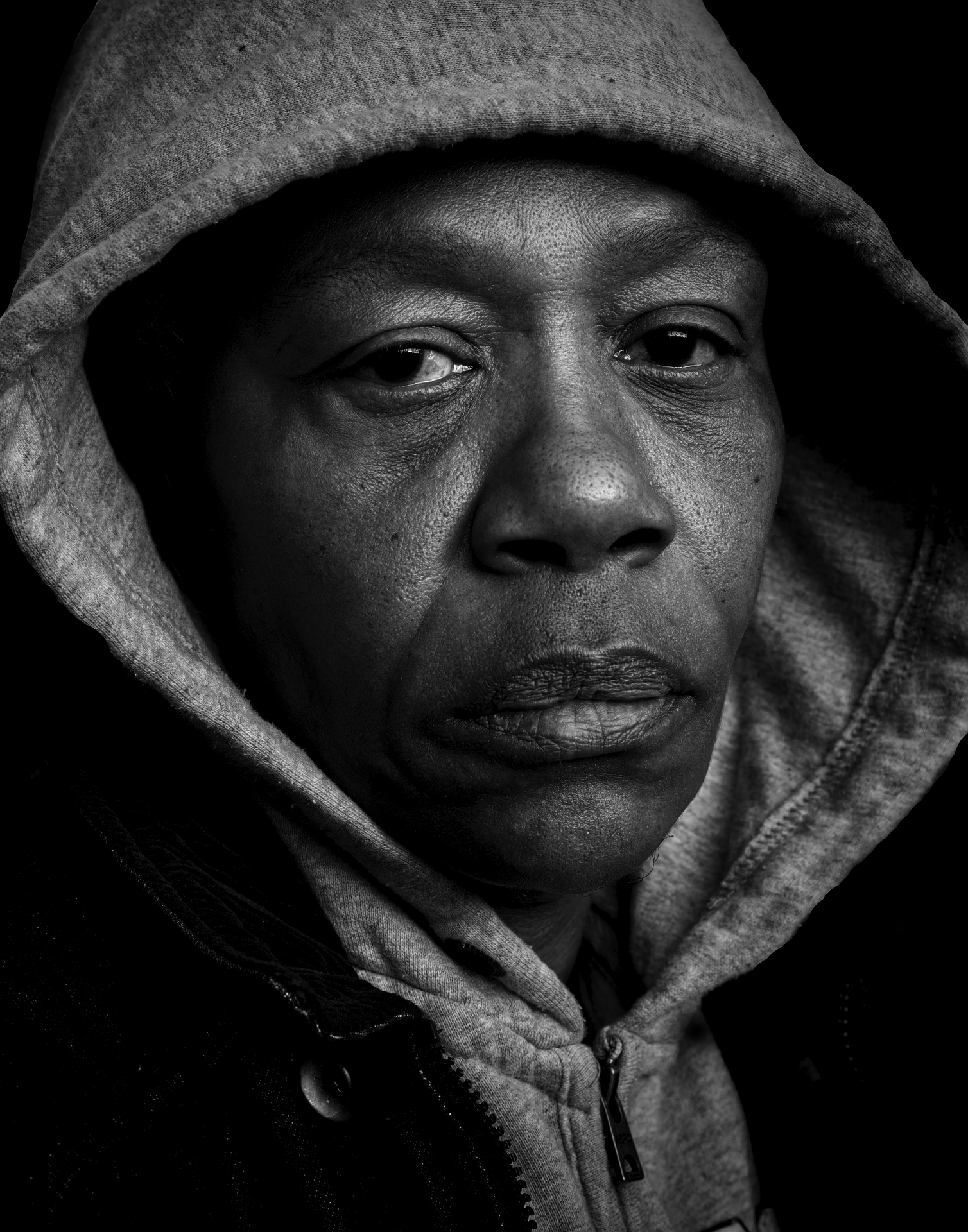 Black and white close-up portrait of a person wearing a hoodie with the hood up, with a serious expression.