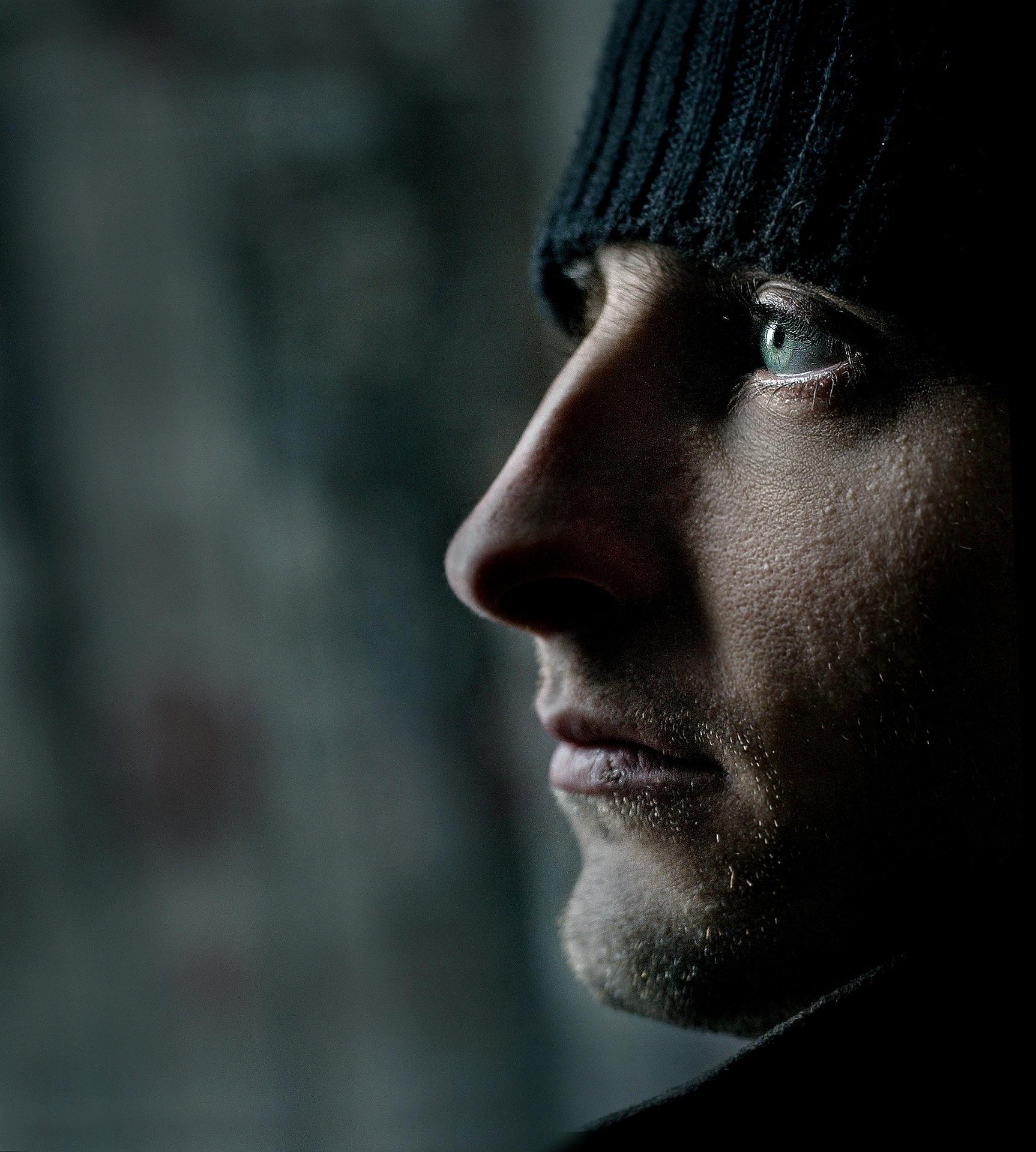 Close-up of a person's face, focusing on their eye and partial profile, wearing a black beanie, with a dark and blurred background.