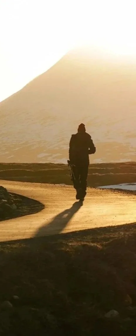 Person walking on a dirt path at sunset with a mountain in the background.