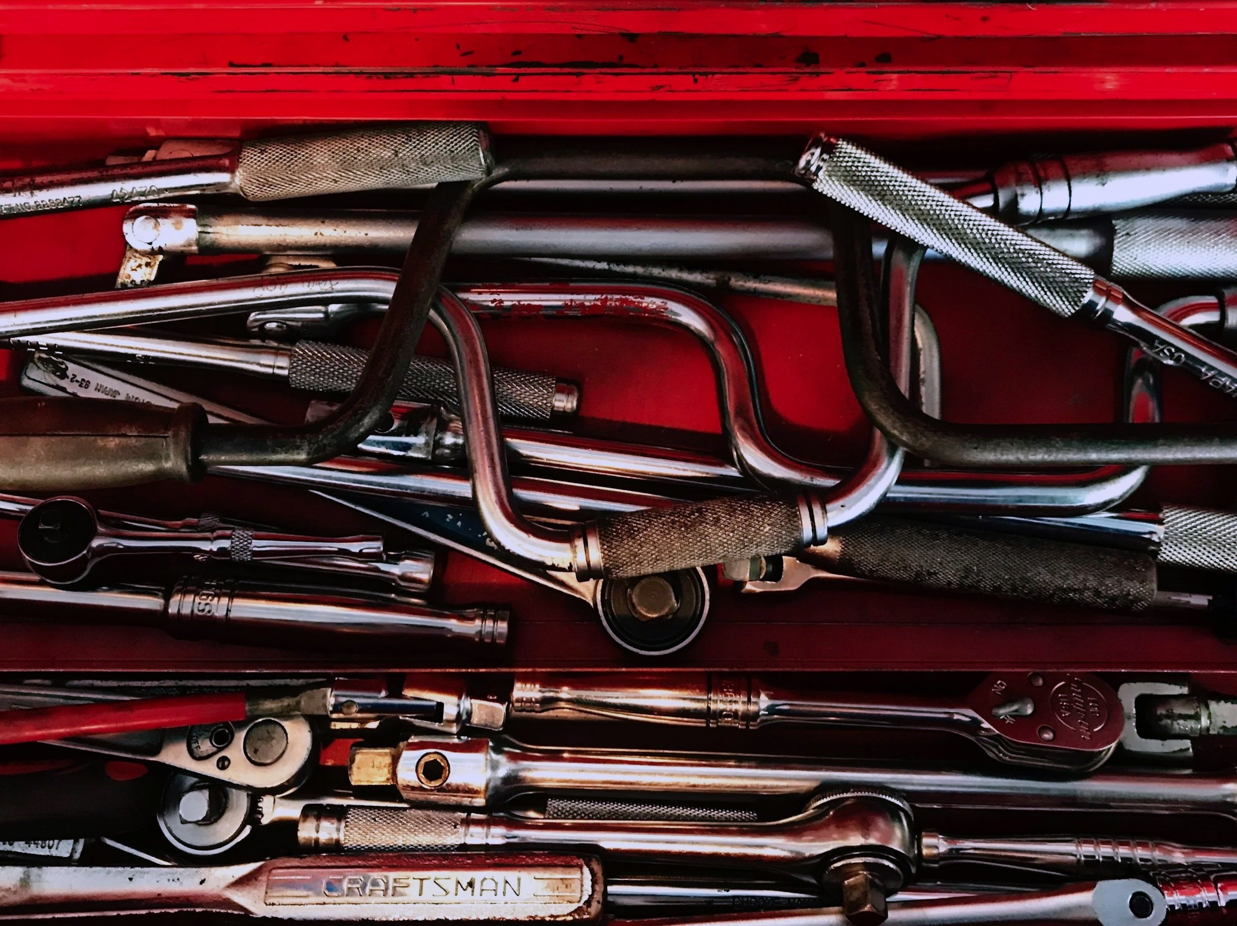 Collection of various metal tools, including extension wrenches, screwdrivers, and a box labeled 'Craftsman,' stacked in a red container.