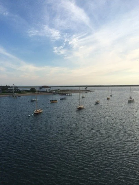 Nantucket harbor with several sailboats anchored on calm water under a partly cloudy sky.
