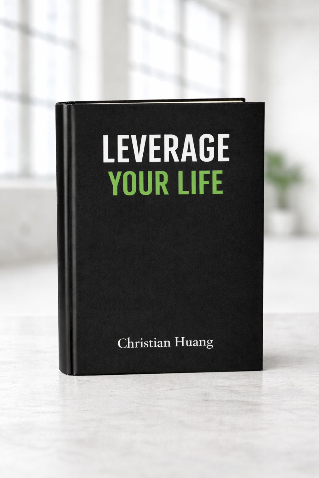 Black book titled "Leverage Your Life" by Christian Huang on a white surface with a blurred background of a window and plant.