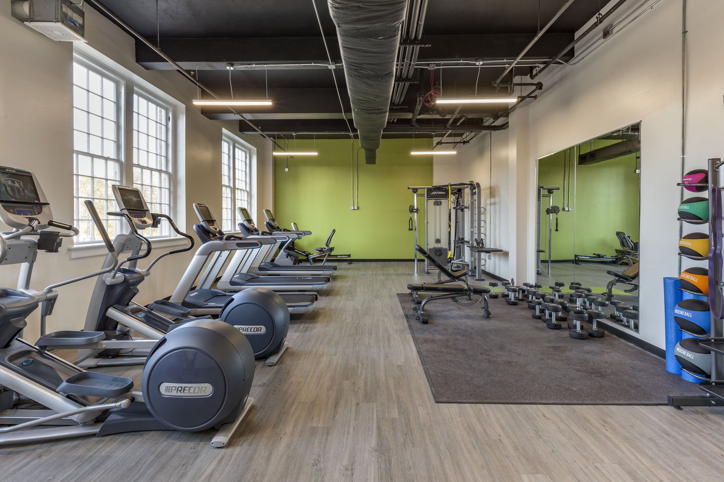 Indoor gym with treadmills, elliptical machines, weightlifting equipment, free weights, and resistance balls.