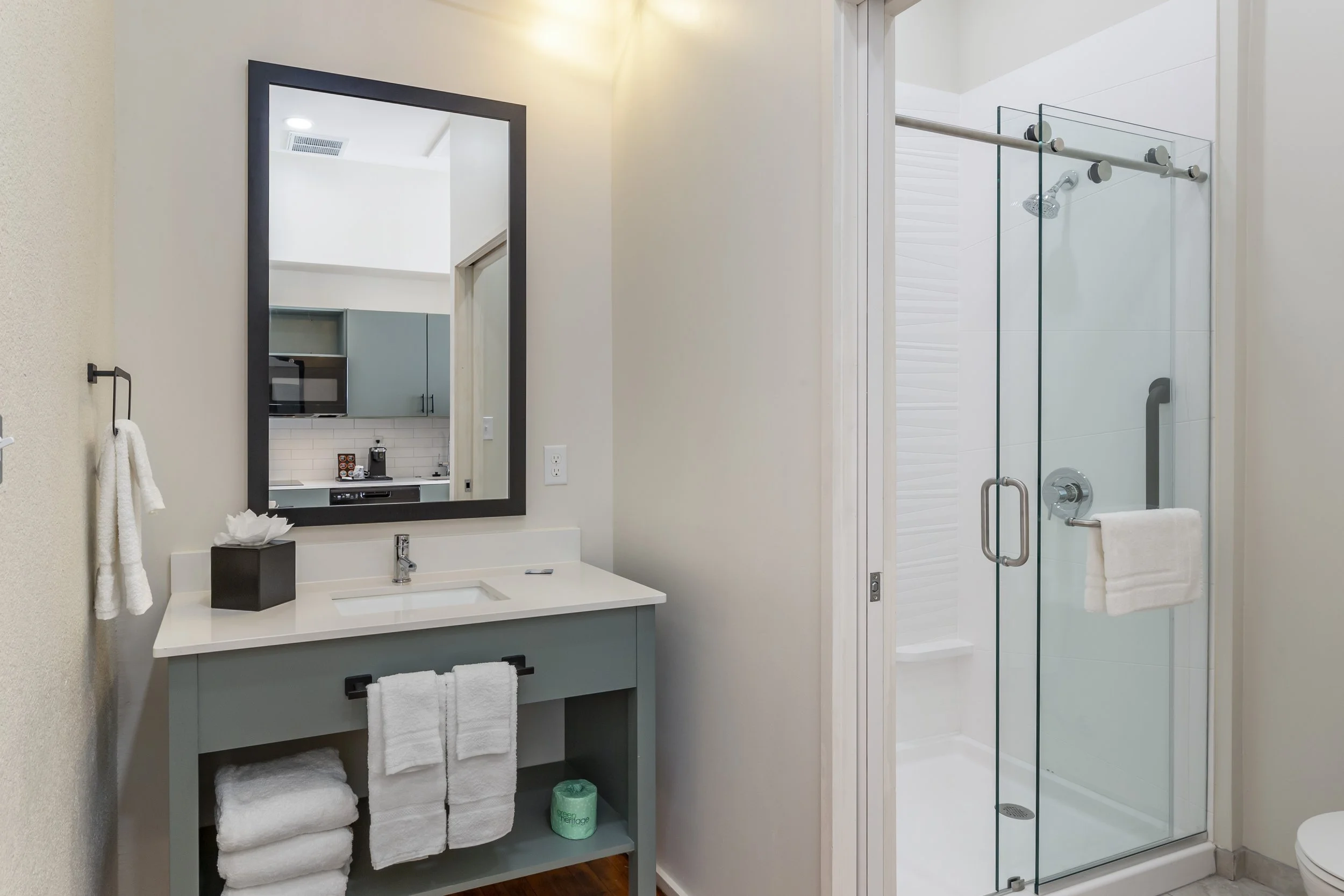 Modern bathroom with a light green vanity, a mirror, towels, and a glass-enclosed shower.