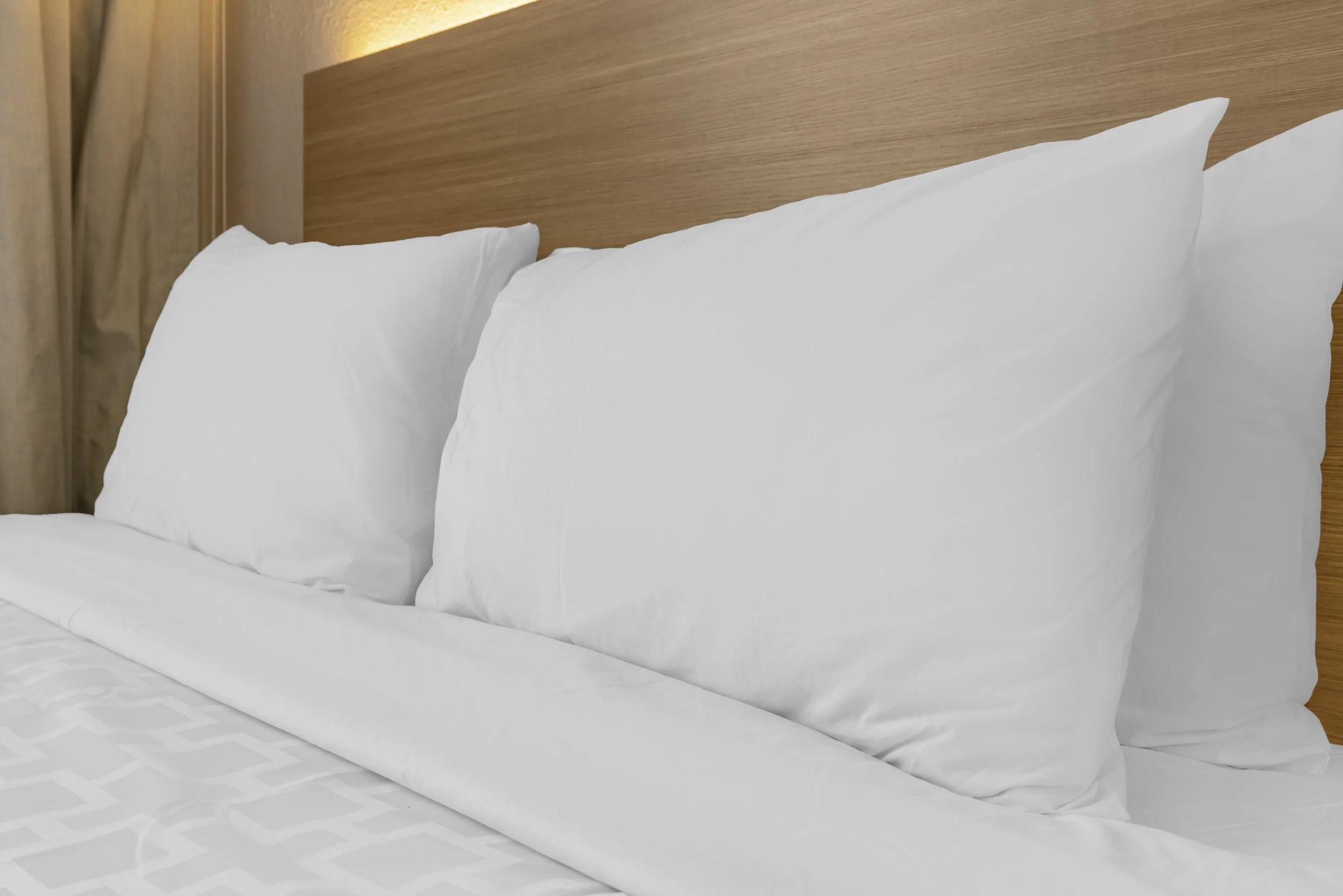 Close-up of neatly made bed with white pillows, bedsheets, and a wooden headboard.