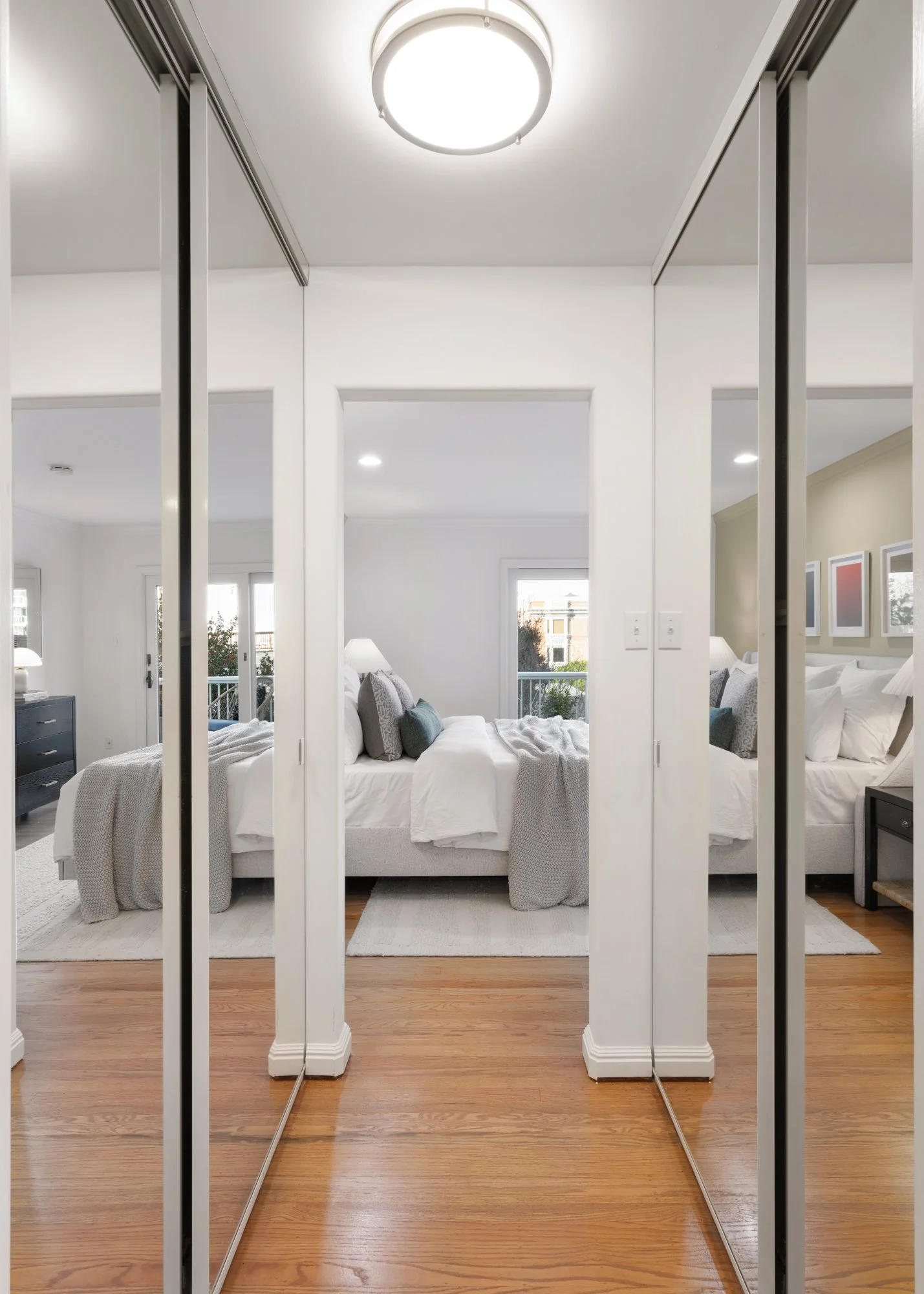 Mirror closet doors reflecting a bedroom with two beds, white bedding, and nightstands with lamps, in a bright, modern room.