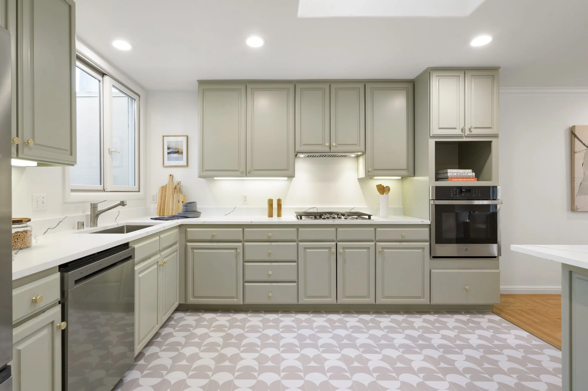 Modern kitchen with light gray cabinets, white marble countertops, patterned tile floor, stainless steel appliances, and a window above the sink.