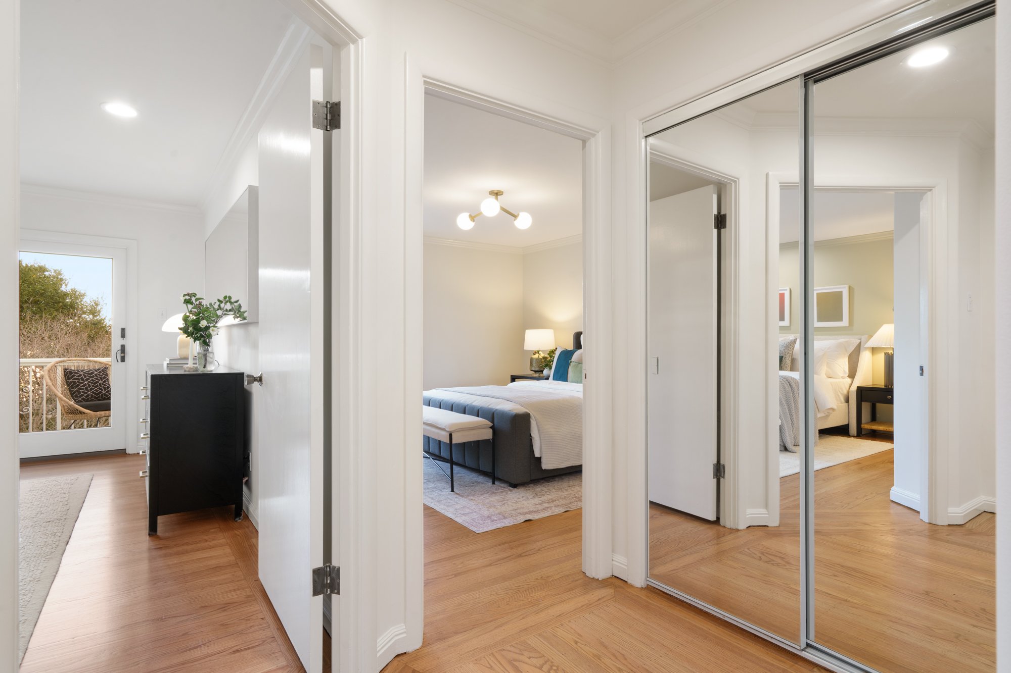 View of a hallway leading to two bedrooms with hardwood floors, and a mirrored closet door on the right.