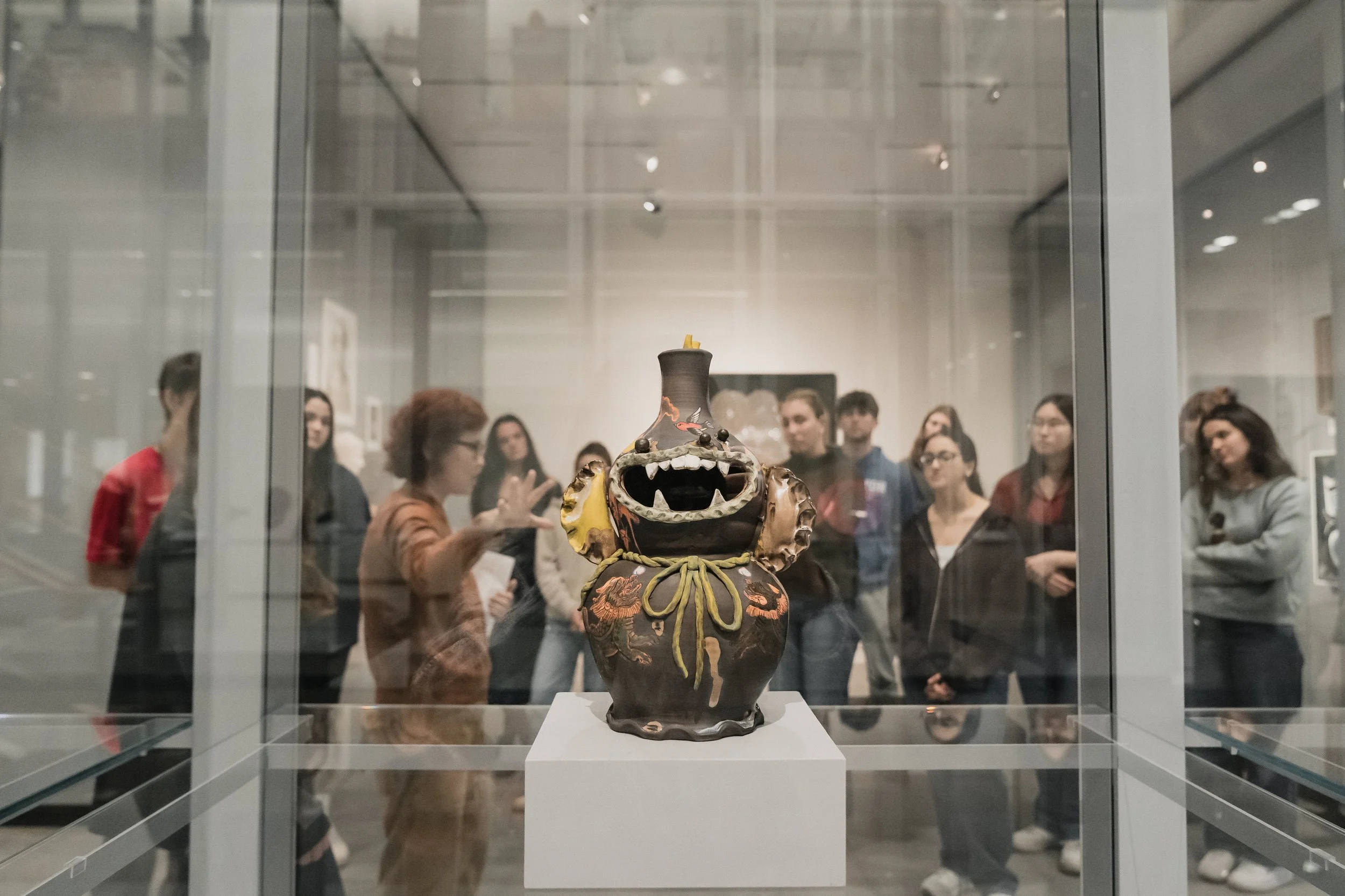 A decorative ceramic vase with a dragon design inside a glass display case in a museum, with visitors observing in the background.