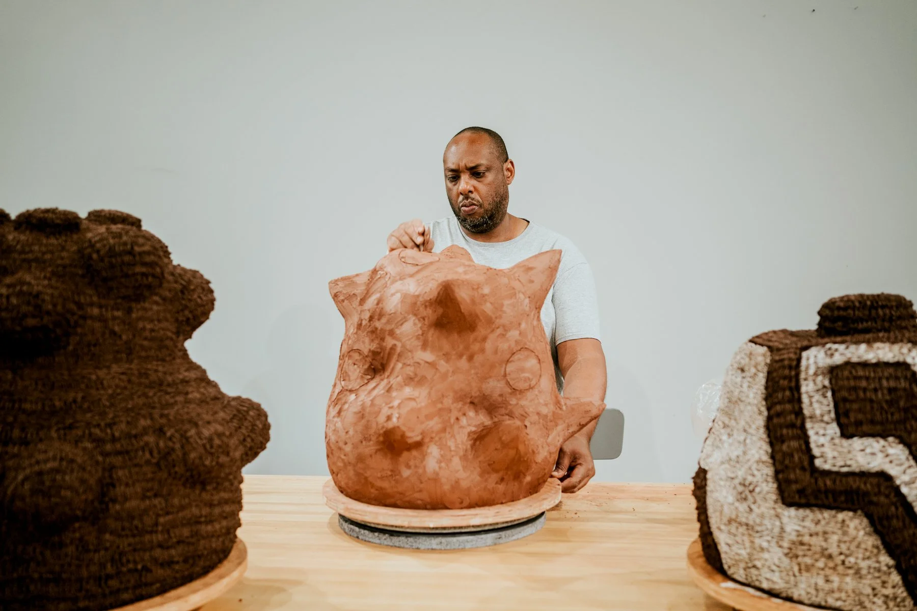 A man inspecting a large, textured terracotta sculpture surrounded by rolled knitted fabrics on a table.