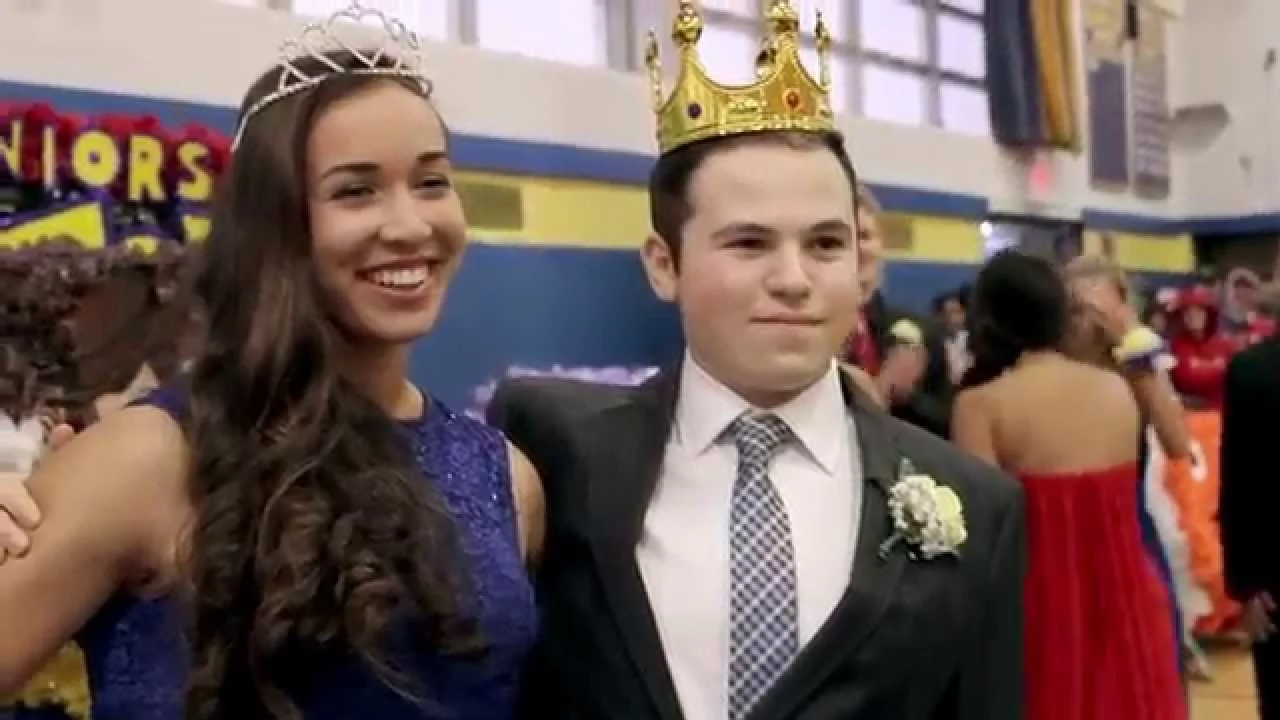 Young woman and young man dressed formally at a school dance, the young woman with a tiara and the young man with a gold crown and boutonnière.