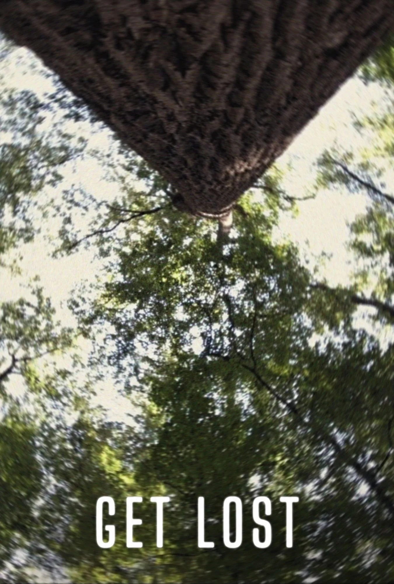 Upside-down view of a massive textured tree trunk surrounded by leafy branches and sky, with bold white text reading “GET LOST,” evoking adventure.