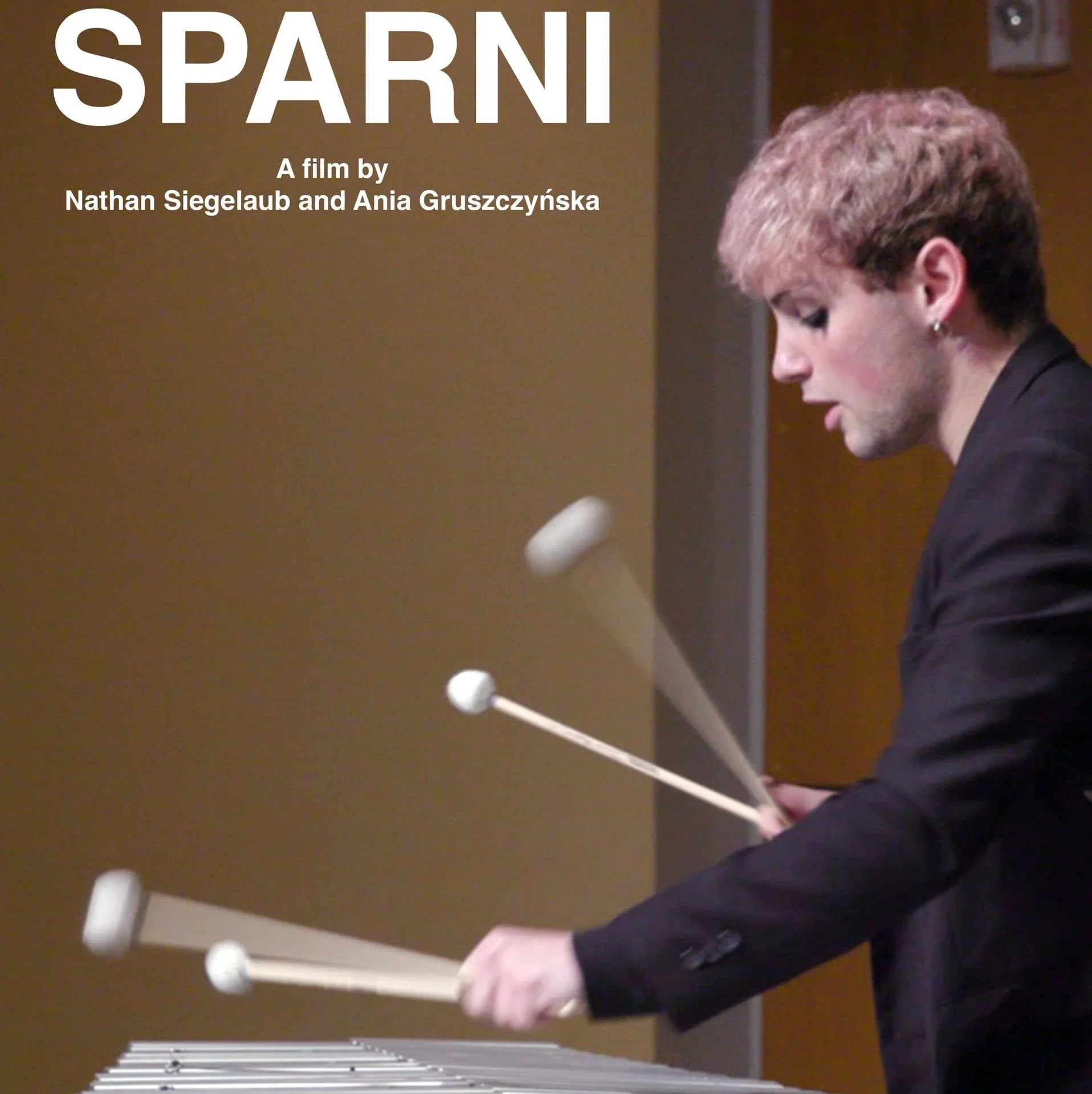 A person focused on playing a xylophone with precision, using four mallets. The background is neutral, highlighting the intensity. Text reads “SPARNI, A film by Nathan Siegelaub and Ania Gruszczyńska.”