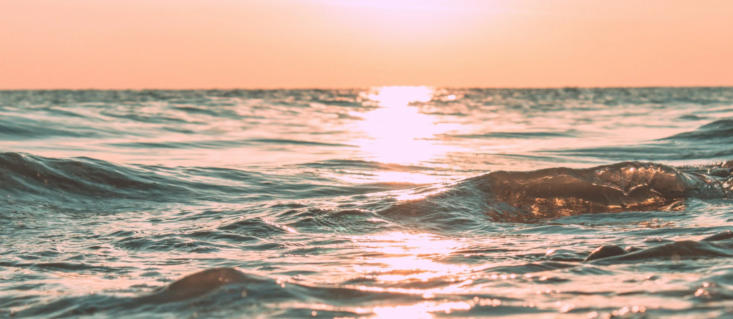 Sunset over the ocean with gentle waves and the sun reflecting on the water's surface