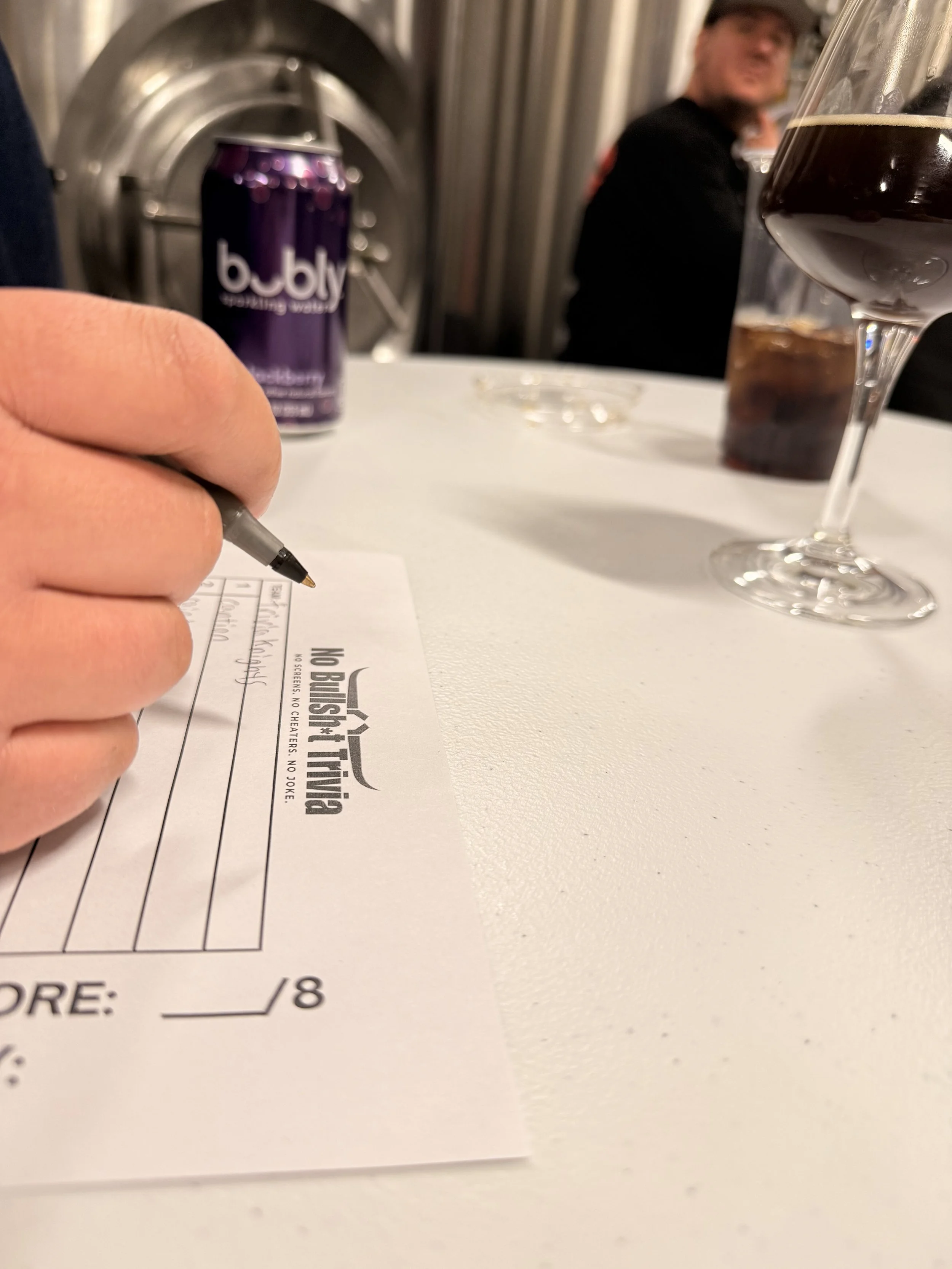 A photograph of a player writing their answers on a No Bullshit Trivia answer sheet
