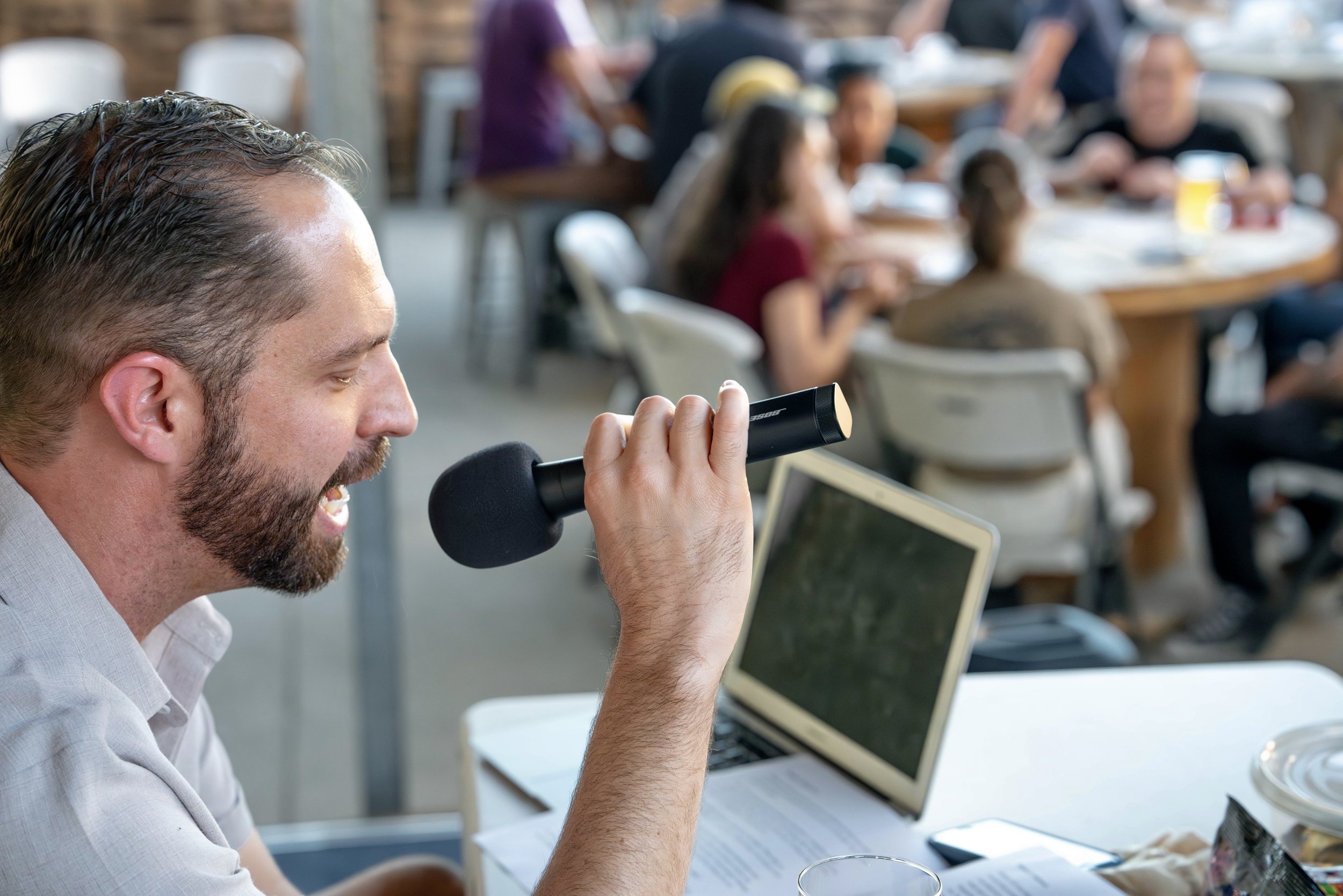 A photo of James, one of the creators of No Bullshit Trivia. He is reading trivia questions into a microphone.