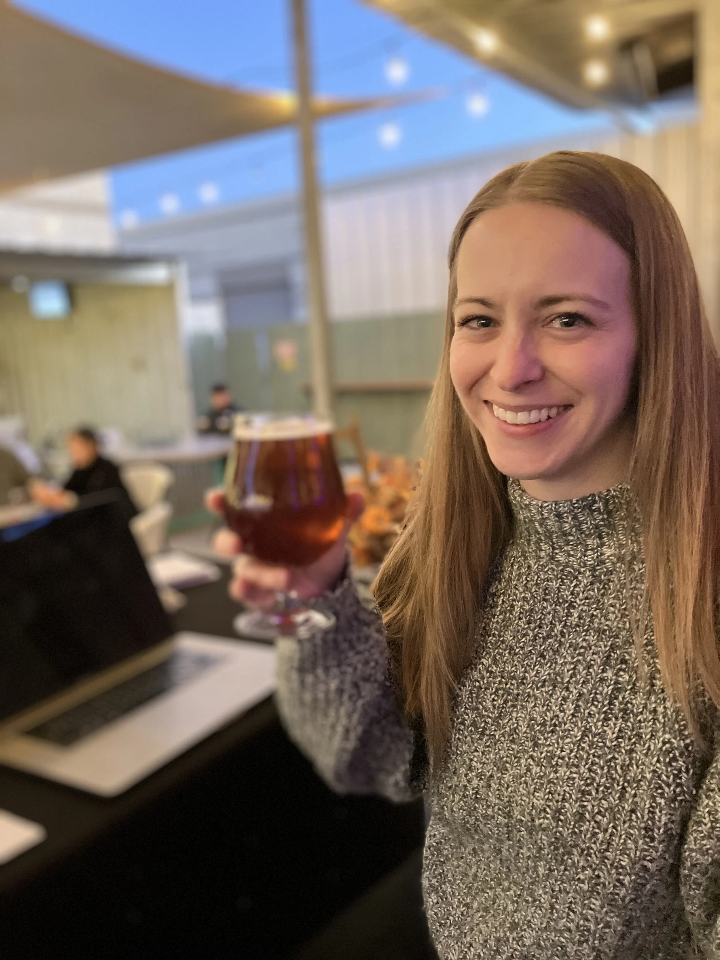 A photograph of Amy, one of the creators of No Bullshit Trivia. She is on stage holding a beer.