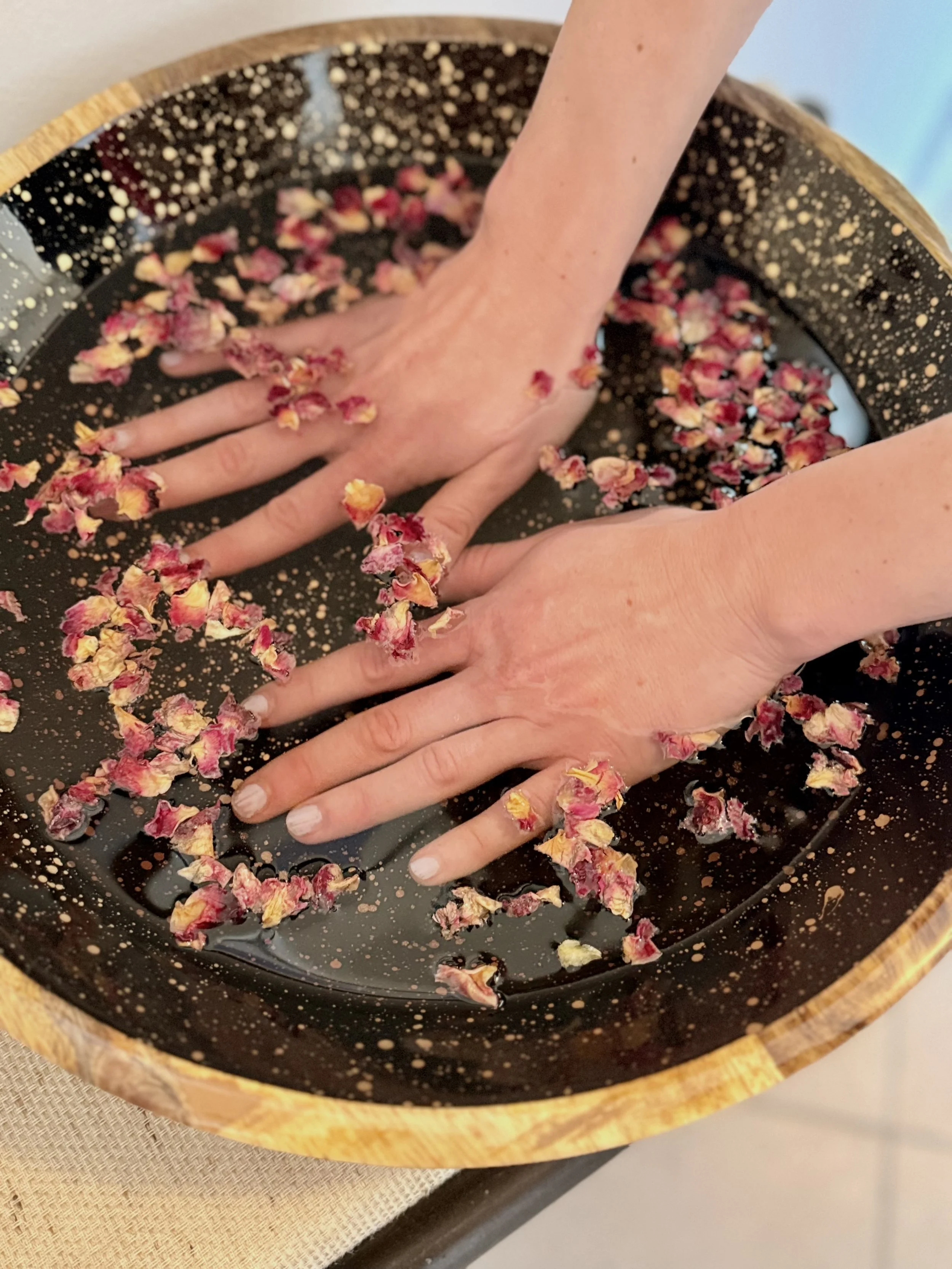 Frauenhände in schwarzer glitzernder Schüssel mit Handbad mit Rosenblättern