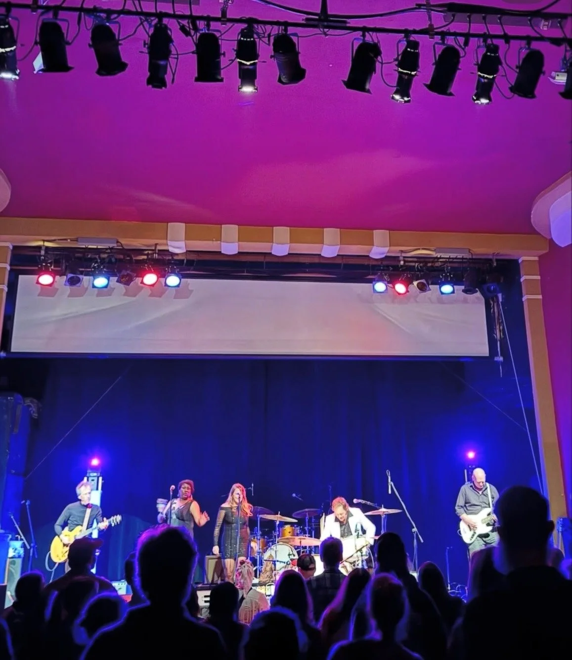 Suite G Studio's Grooveworks Team building informations page featuring musicians performing on a stage with colorful lights, including two vocalists and three instrumentalists, in front of an audience.