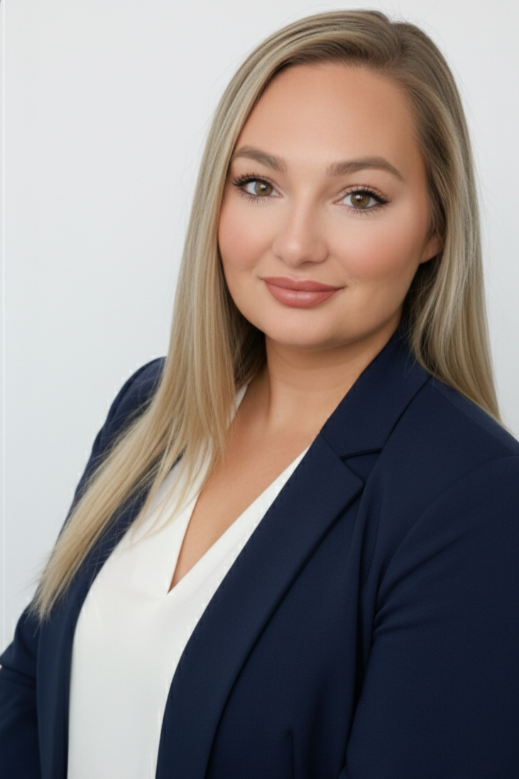 A professional woman with long blonde hair, wearing a navy blazer and white blouse, smiling softly against a plain white background.
