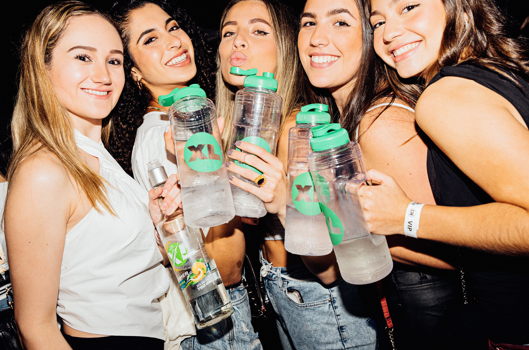 Group of five women smiling and holding water bottles at a party or event.