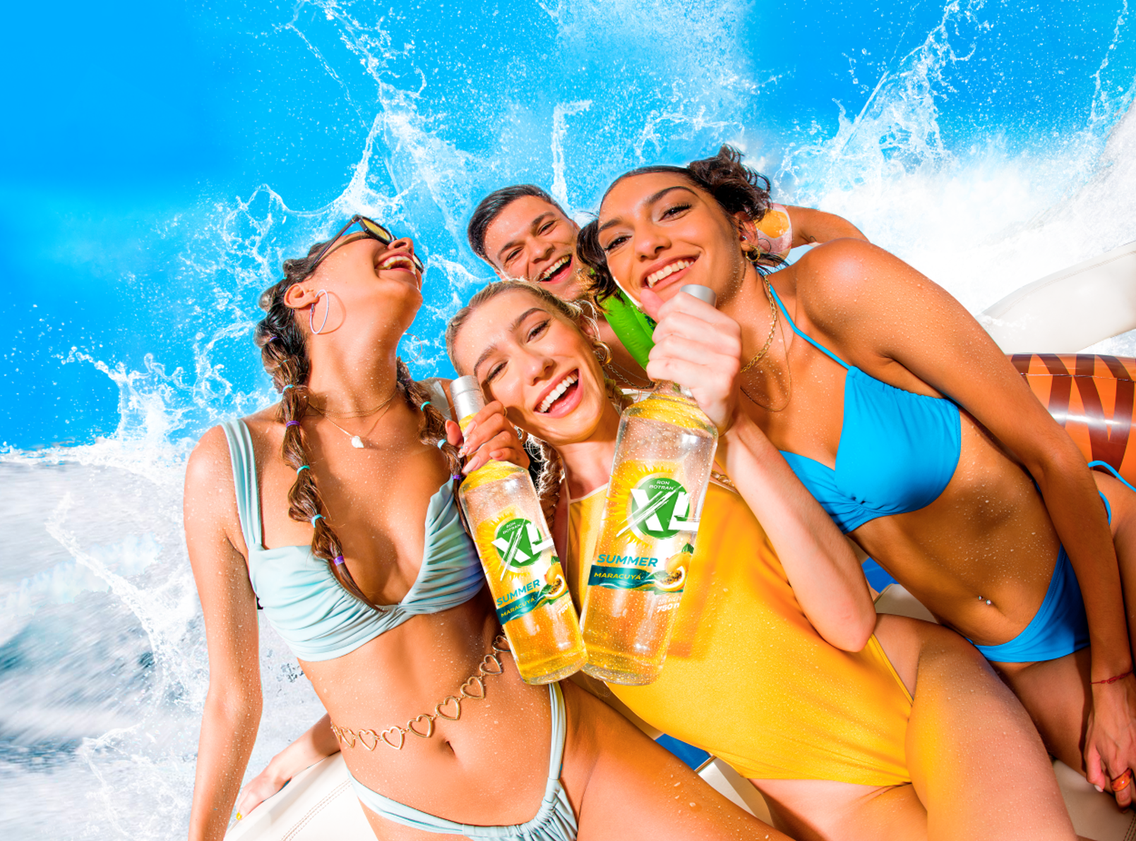 Group of five young women in swimsuits on a boat, smiling, holding bottles of bottled water or soda, with water splashing behind them, enjoying a sunny day.