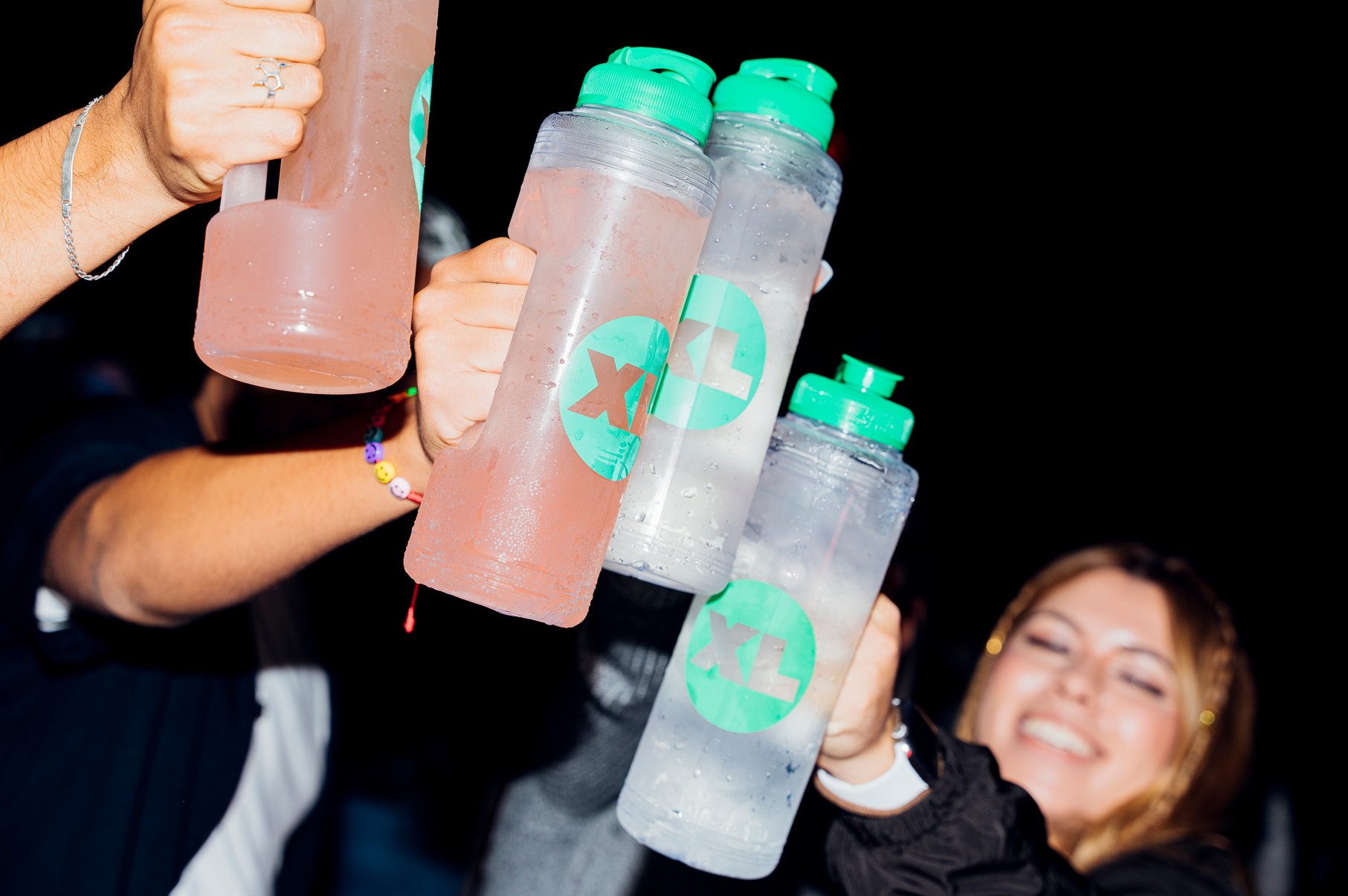 Group of people holding bottles of water or sports drinks with green lids, some bottles labeled with a green and white logo, smiling woman in the background.