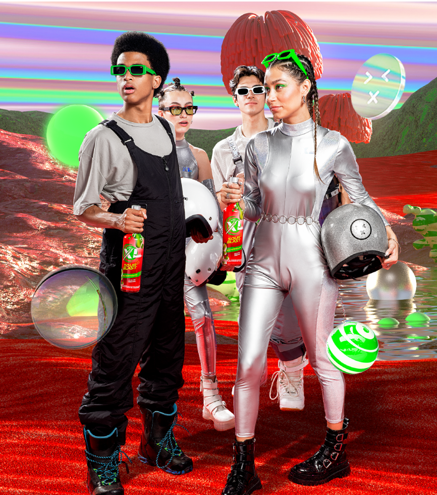 A group of four young people standing on a surreal, colorful landscape with floating spheres and a large red sculptural object in the background, all dressed in futuristic or retro fashion and holding bottles of soda.