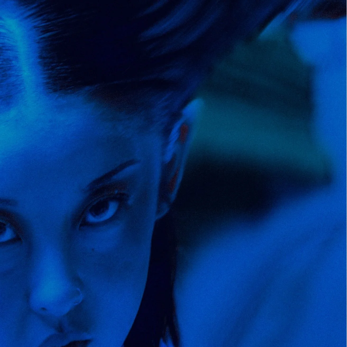 Close-up of a person's face, illuminated with blue lighting, showing eyes, nose, and parted lips with dark hair.