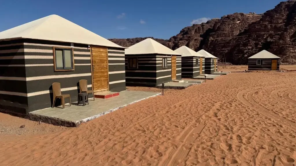Four black and white striped tents with white roofs, situated on concrete platforms in a desert landscape with rocky hills in the background.