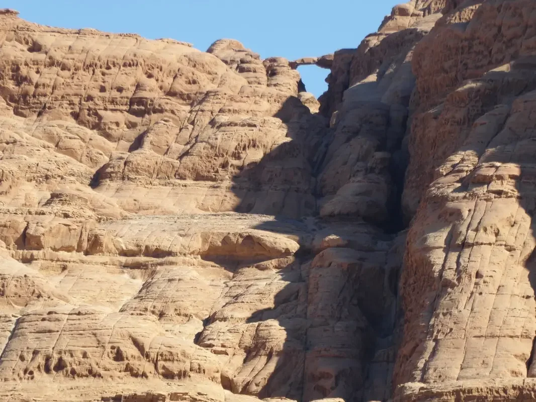 Rock formations in a desert landscape with a natural stone arch in the background, clear blue sky, and sunny weather.