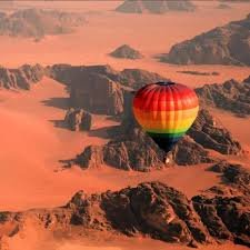 Hot air balloon with rainbow colors flying over a desert canyon landscape at sunset.