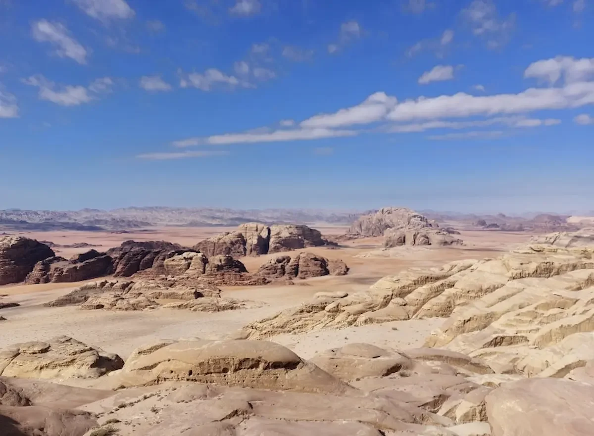 A vast desert landscape with rocky formations under a blue sky with scattered clouds.