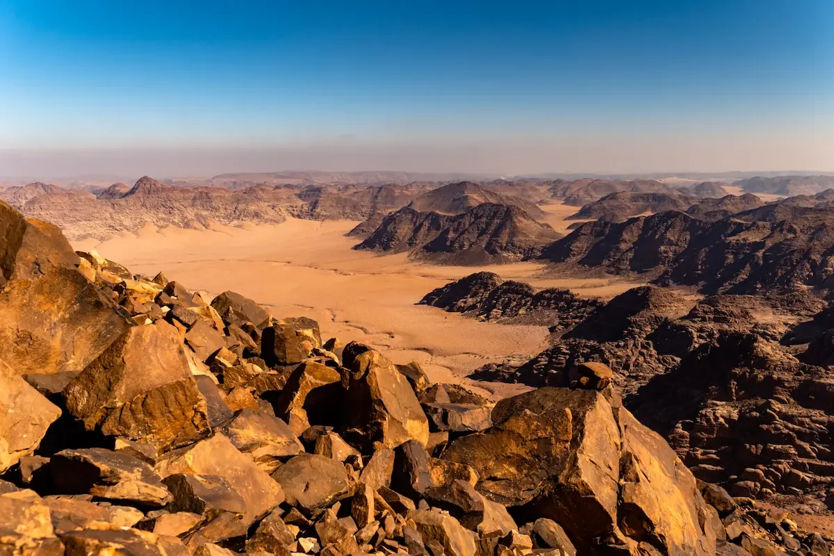 A vast desert landscape with rocky hills and mountains under a clear blue sky.