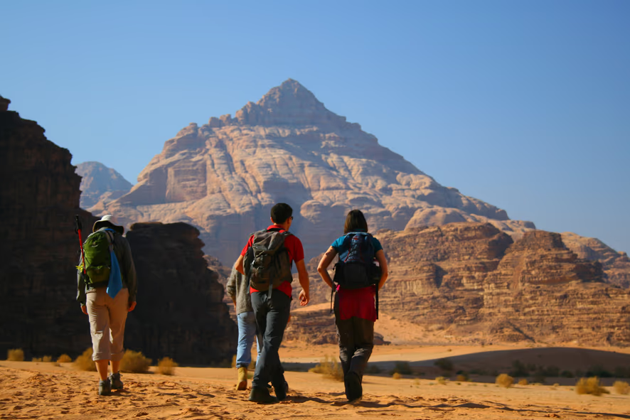 Four hikers walking through a desert landscape towards a mountain in the distance.